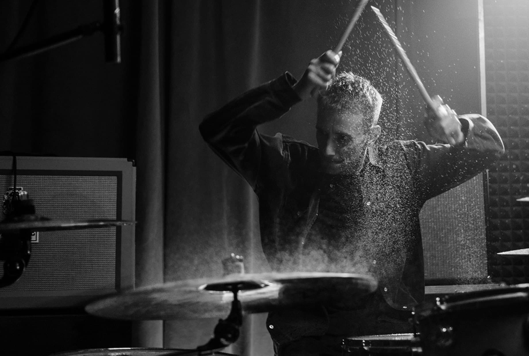 Drummer striking a drum kit during an intense performance.