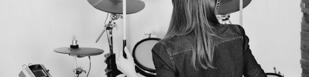 Female drummer playing on an electric drum set in her home studio, practicing essential drumming skills.